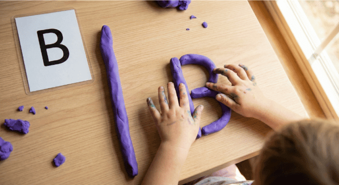 Preschooler forming letter B shape with purple playdough on table