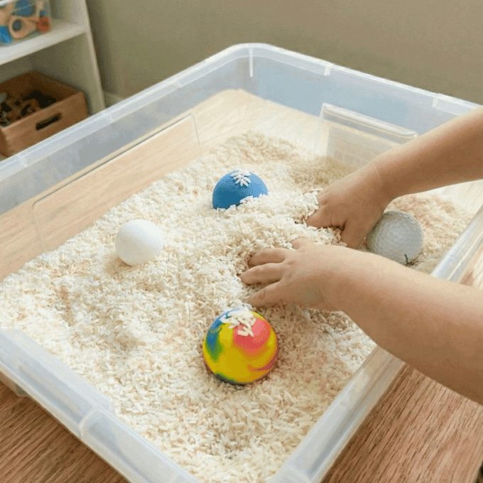 Preschool sensory bin activity with hands finding bouncy balls, ping pong balls, and foam balls in rice