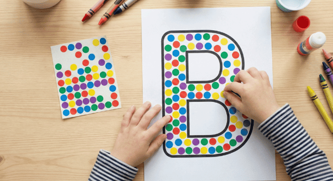 Child filling letter B outline with colorful stickers for fine motor practice