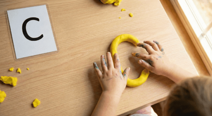 Preschooler forming letter C shape with yellow playdough on table