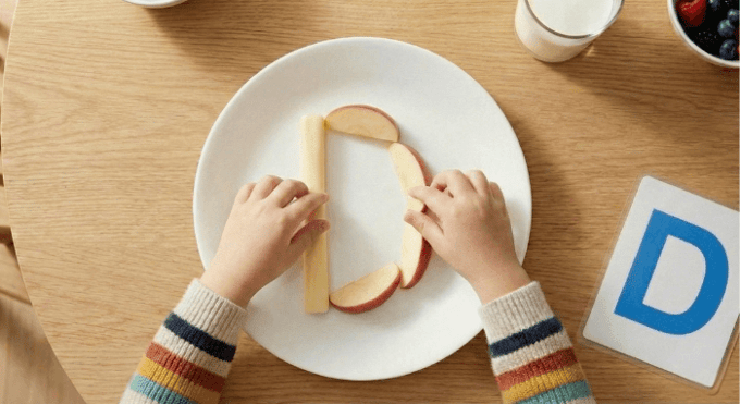 Preschooler forming letter D shape with cheese stick and apple slices for edible learning activity