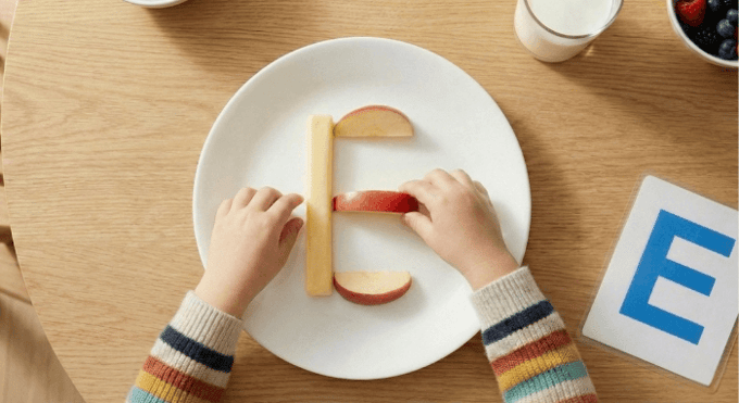 Preschooler forming letter E shape with cheese stick and apple slices for edible learning activity