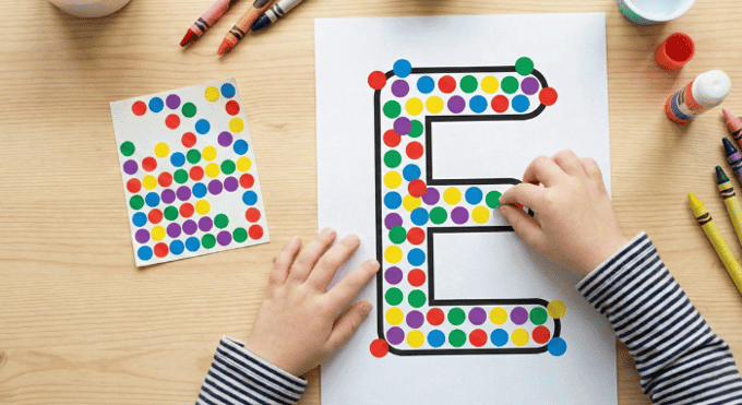 Child filling letter E outline with colorful stickers for fine motor practice
