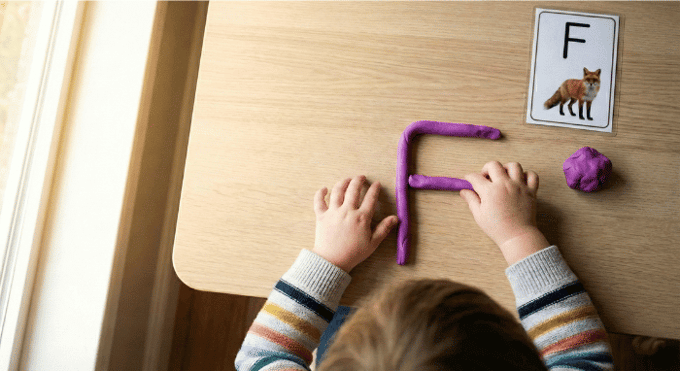 Preschooler forming letter F shape with purple playdough on table