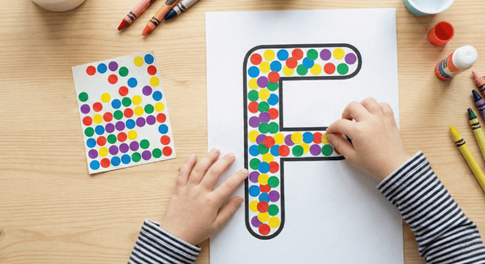 Child filling letter F outline with colorful stickers for fine motor practice