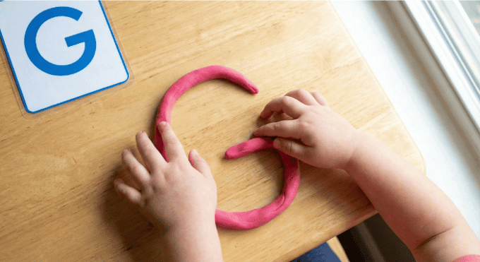Preschooler forming letter G shape with pink playdough on table