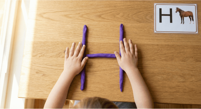 Preschooler forming letter H shape with purple playdough on table