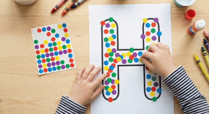 Child filling letter H outline with colorful stickers for fine motor practice