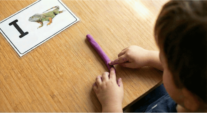 Preschooler forming letter I shape with purple playdough on table