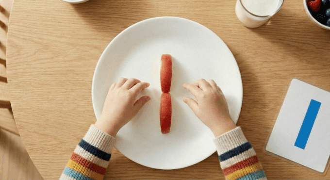 Preschooler forming letter I shape with apple slices for edible learning activity