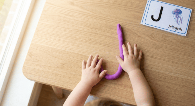 Preschooler forming letter J shape with purple playdough on table