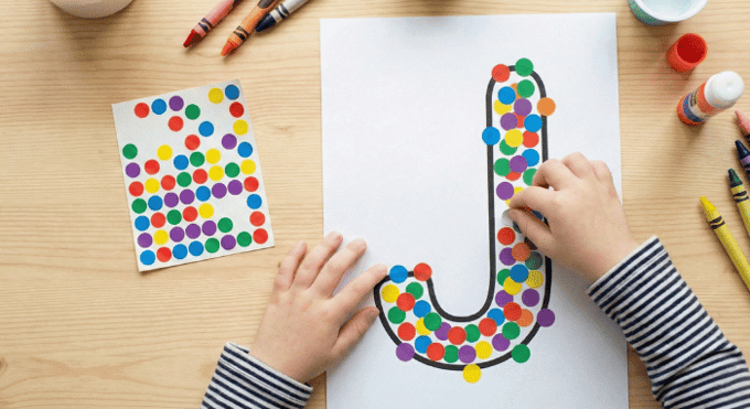 Child filling letter J outline with colorful stickers for fine motor practice