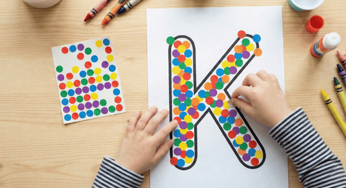 Child filling letter K outline with colorful stickers for fine motor practice