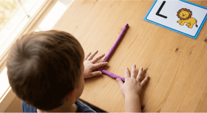 Preschooler forming letter L shape with purple playdough on table