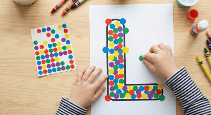 Child filling letter L outline with colorful stickers for fine motor practice
