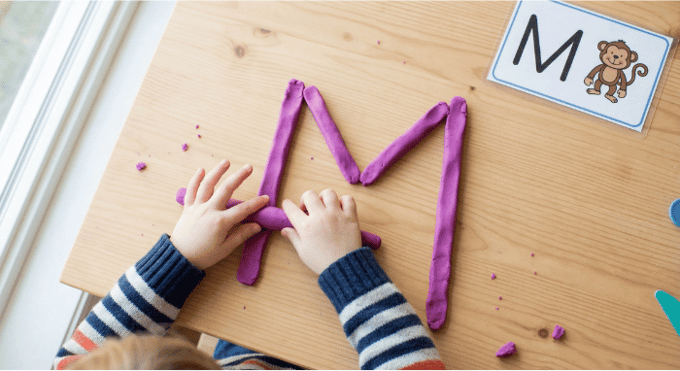 Preschooler forming letter M shape with purple playdough on table