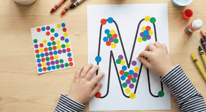Child filling letter M outline with colorful stickers for fine motor practice