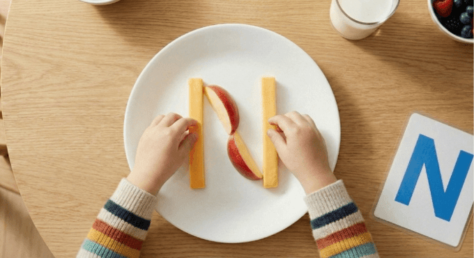 Preschooler forming letter N shape with cheese stick and apple slices for edible learning activity