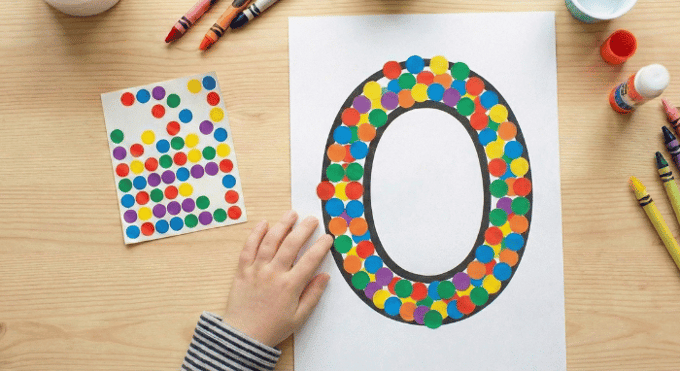 Child filling letter O outline with colorful stickers for fine motor practice