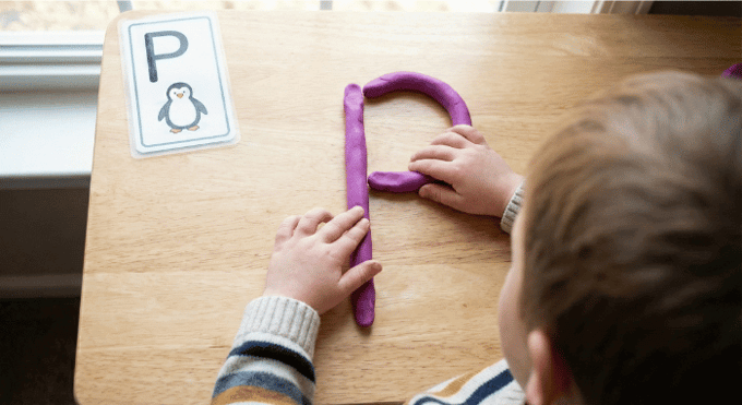 Preschooler forming letter P shape with purple playdough on table