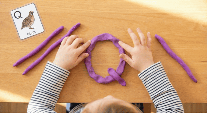 Preschooler forming letter Q shape with purple playdough on table