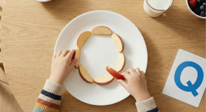 Preschooler forming letter Q shape with apple slices for edible learning activity