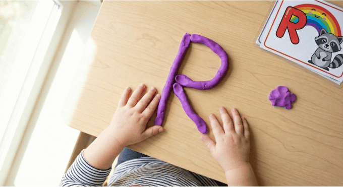 Preschooler forming letter R shape with purple playdough on table