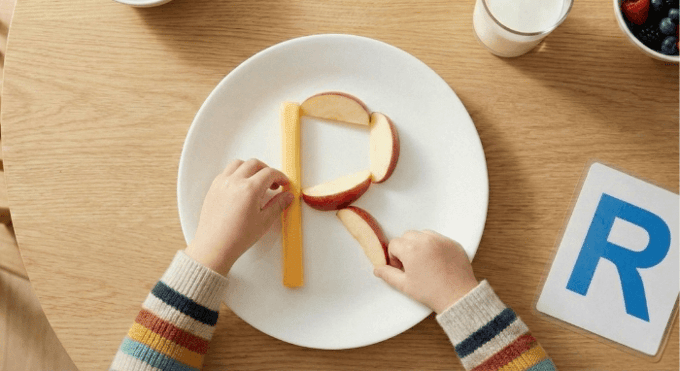 Preschooler forming letter R shape with cheese stick and apple slices for edible learning activity