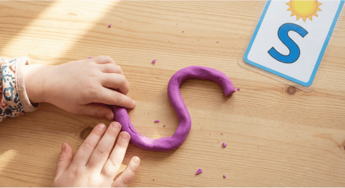 Preschooler forming letter S shape with purple playdough on table