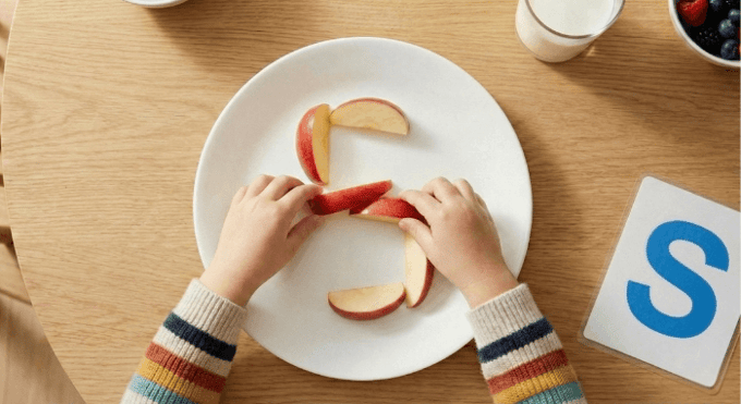 Preschooler forming letter S shape with apple slices for edible learning activity