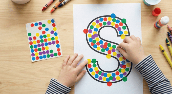 Child filling letter S outline with colorful stickers for fine motor practice