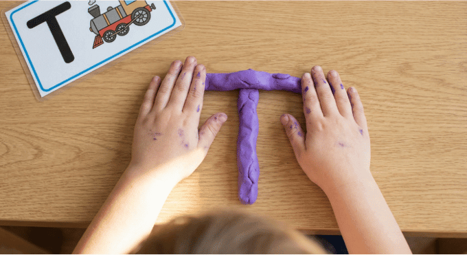 Preschooler forming letter T shape with purple playdough on table