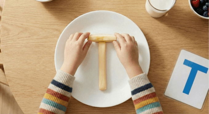 Preschooler forming letter T shape with cheese stick and apple slices for edible learning activity