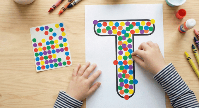 Child filling letter T outline with colorful stickers for fine motor practice