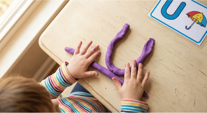 Preschooler forming letter U shape with purple playdough on table