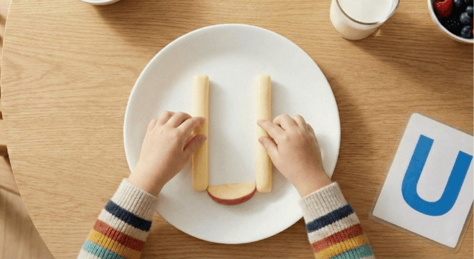 Preschooler forming letter U shape with cheese stick and apple slices for edible learning activity