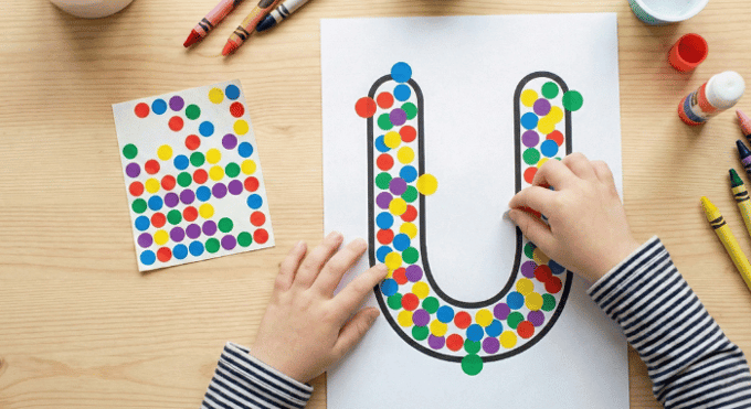 Child filling letter U outline with colorful stickers for fine motor practice