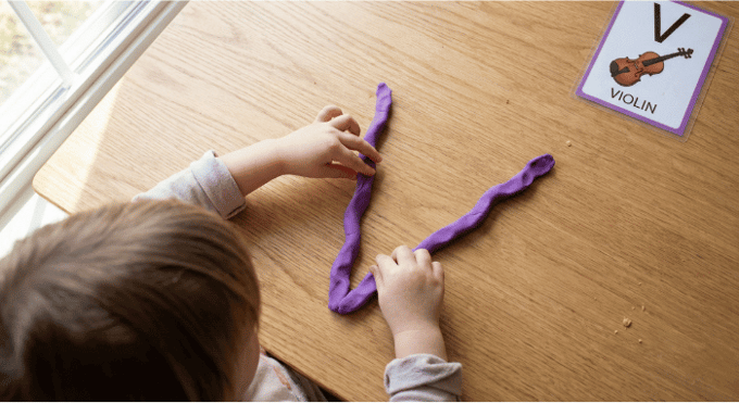 Preschooler forming letter V shape with purple playdough on table