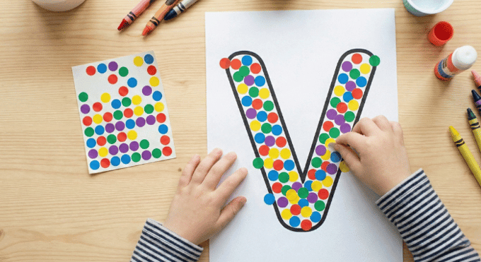 Child filling letter V outline with colorful stickers for fine motor practice