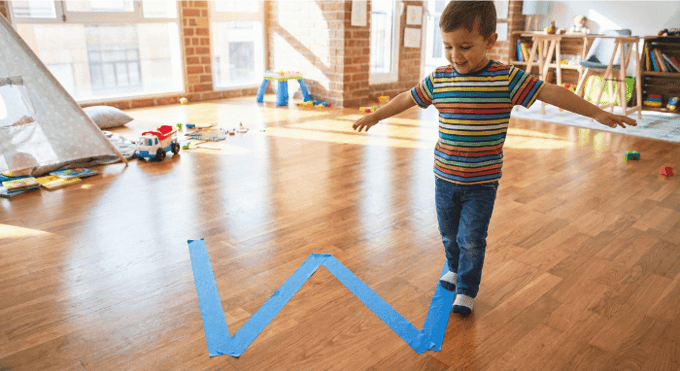 Preschooler hopping on letter W made with tape on floor for active learning