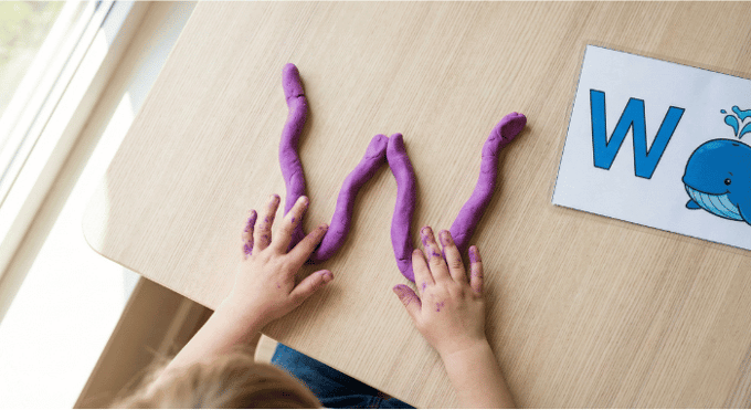 Preschooler forming letter W shape with purple playdough on table