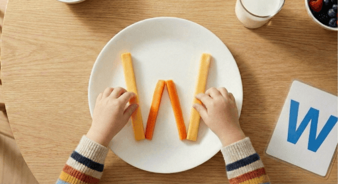 Preschooler forming letter W shape with cheese sticks and carrot sticks for edible learning activity