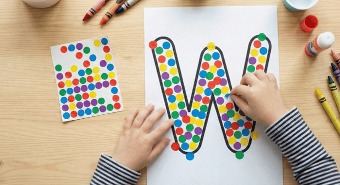 Child filling letter W outline with colorful stickers for fine motor practice