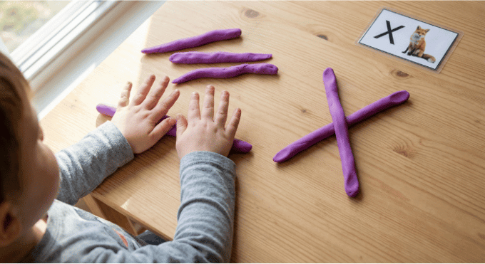 Preschooler forming letter X shape with purple playdough on table