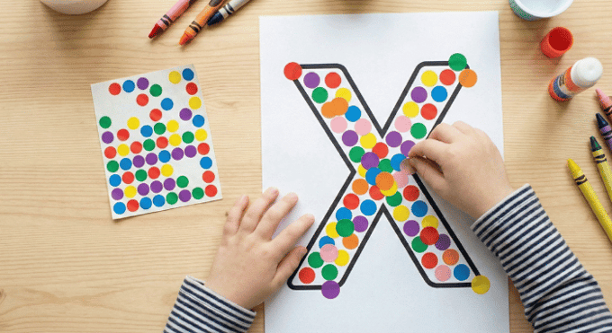 Child filling letter X outline with colorful stickers for fine motor practice