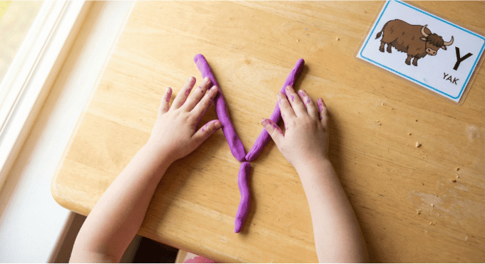 Preschooler forming letter Y shape with purple playdough on table