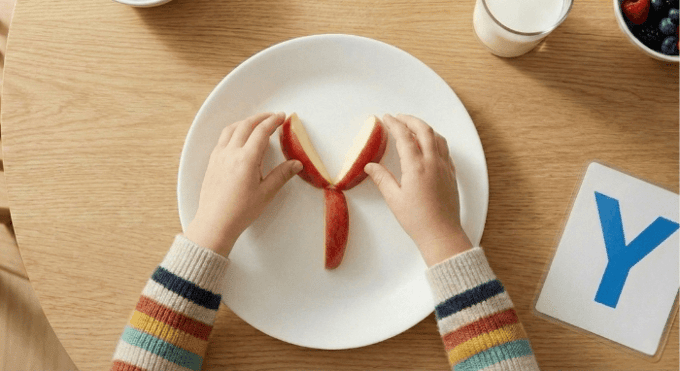 Preschooler forming letter Y shape with apple slices for edible learning activity