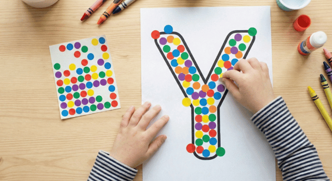 Child filling letter Y outline with colorful stickers for fine motor practice