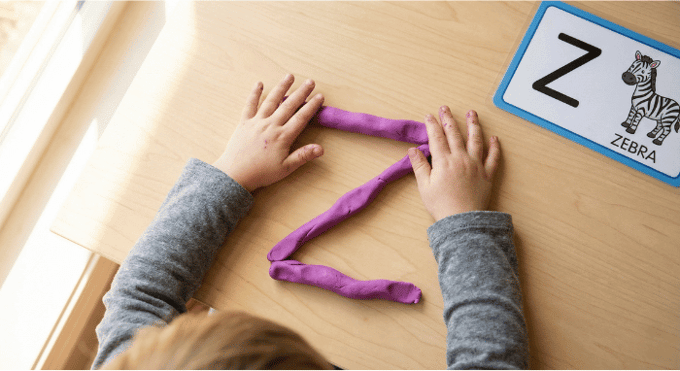 Preschooler forming letter Z shape with purple playdough on table