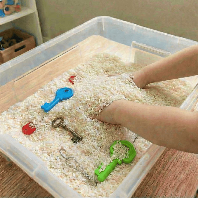 Preschool sensory bin activity with hands finding various real and toy keys in rice